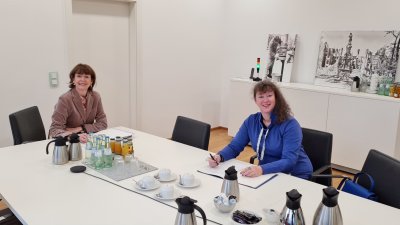 Staatssekretärin Andrea Milz in blauer Strickjacke sitzt mit einer Dame der Stadt Köln an einem Tisch.