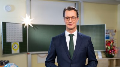 Ministerpräsident Hendrik Wüst steht in einem Klassenraum und spricht in die Kamera