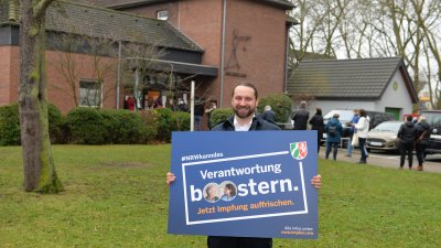 Ein man hält ein Plakat der Booster-Impfkampagne hoch