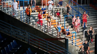 Mehrere Sportlerinnen und Sportler aus vershiedenen Sportartenstehen in ihrer Sportkleidung verteilt auf einer Tribüne. Manche haben einen Ball dabei, ganz unten steht ein Sportler mit seinem Fahrrad.