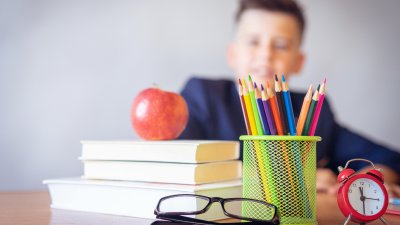 Kind schaut auf Schreibtisch mit Büchern und Stiften